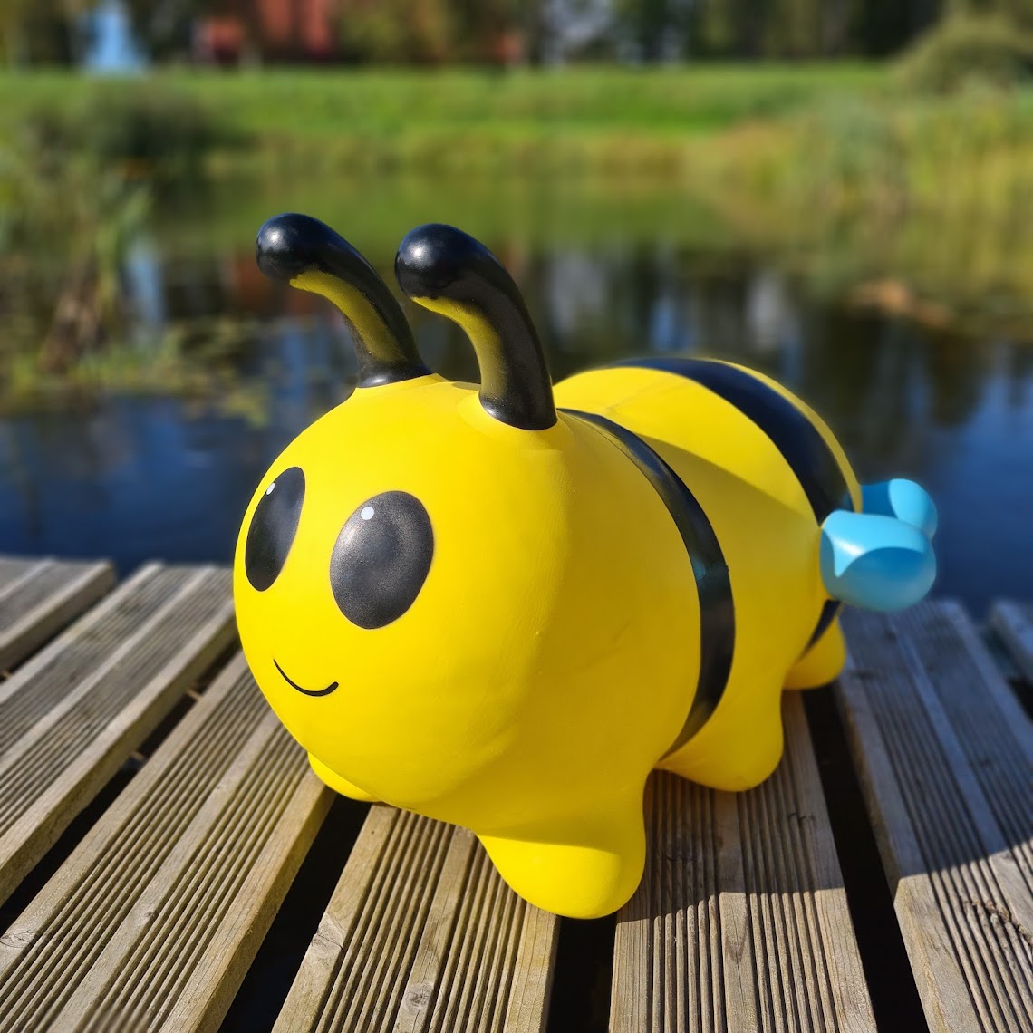 a smiling toddler bouncing on a yellow bee hopper toy in a sunny garden