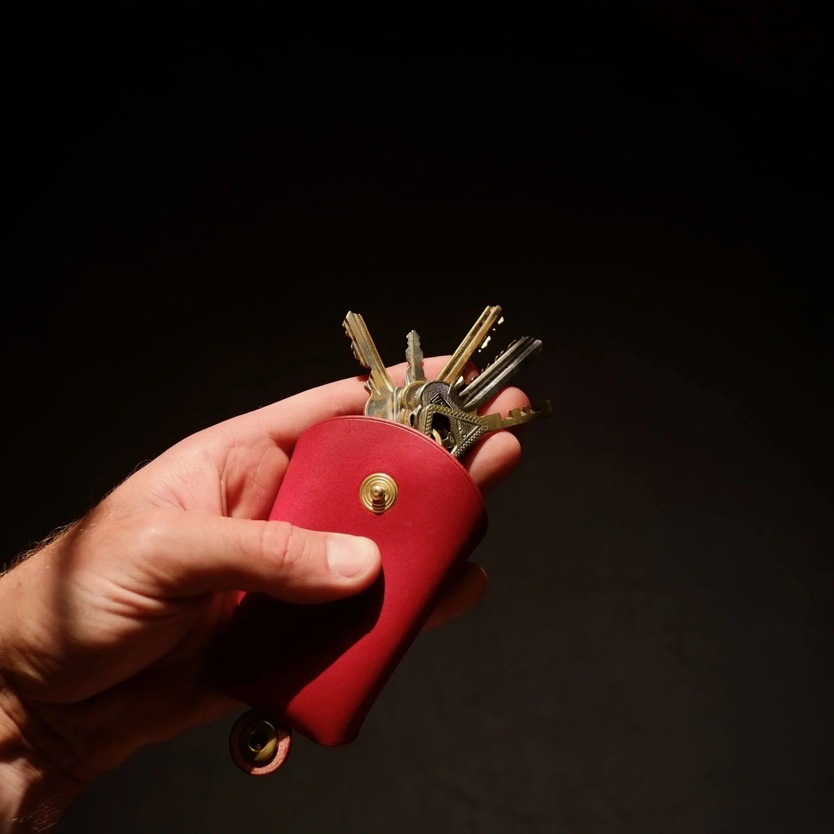 softly lit red leather keyholder held gently in hand, showcasing its comforting texture