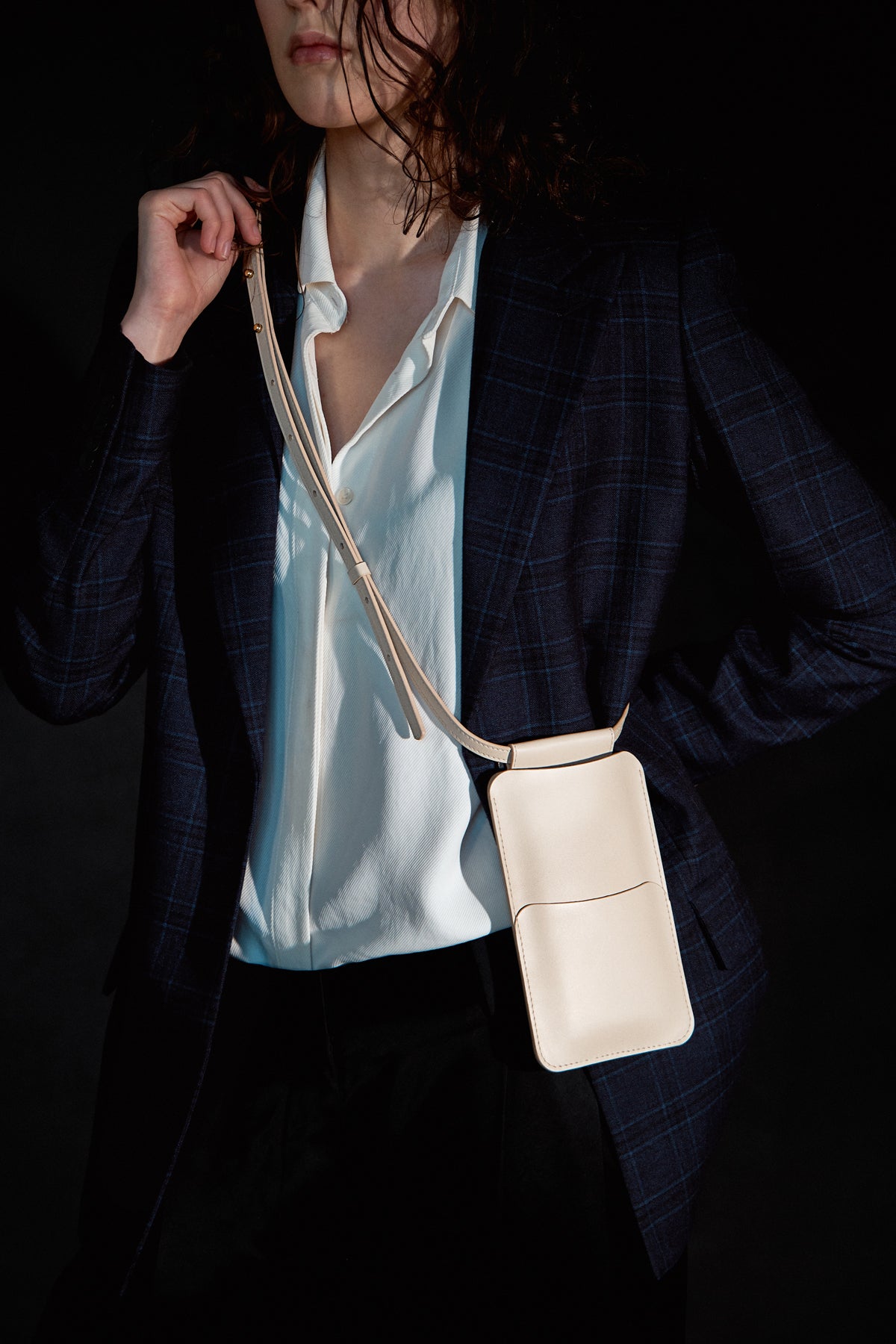 beige leather crossbody phone bag with gold buttons in bold studio light