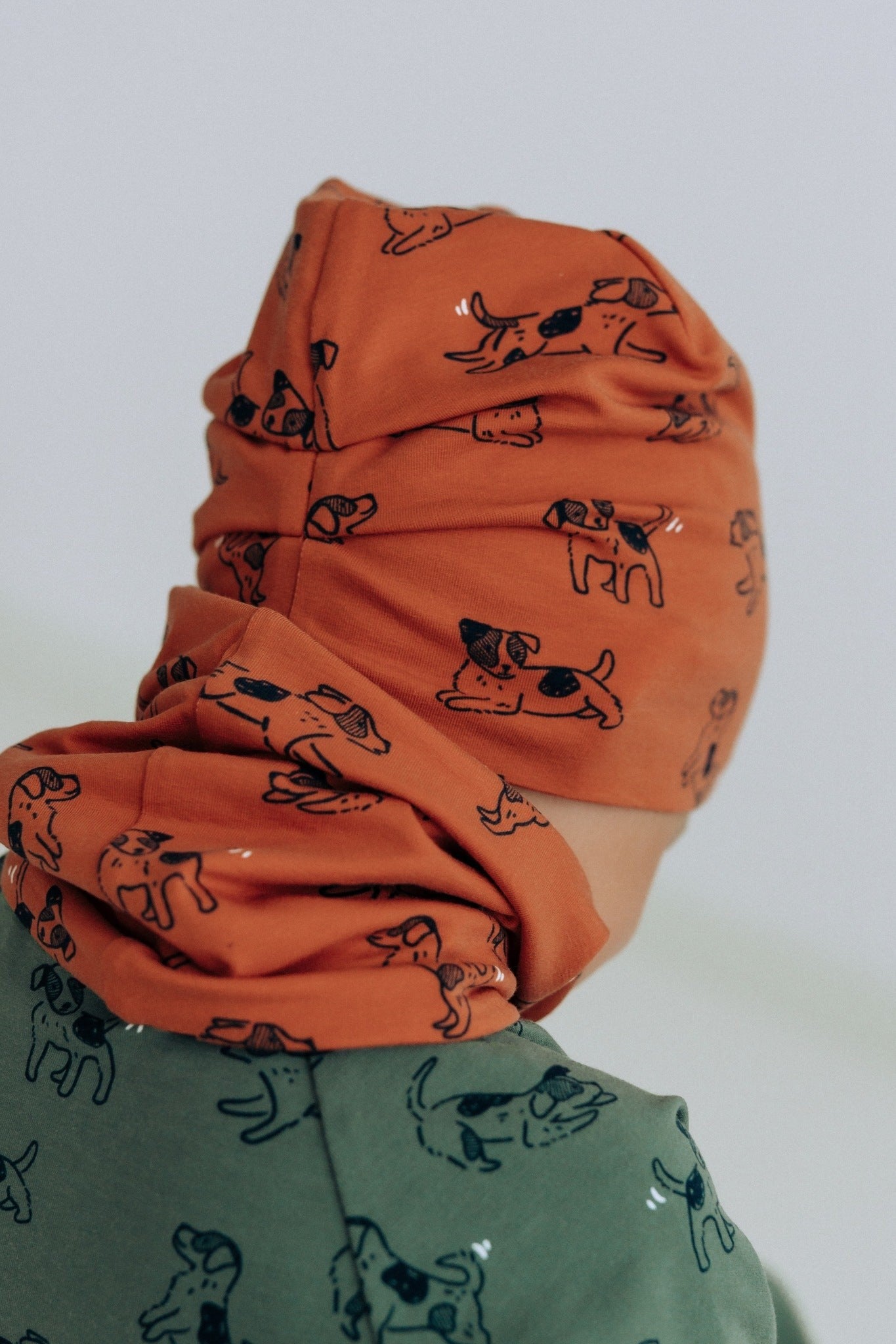 a playful toddler in a copper dogs beanie peeking out from behind a tree on an autumn day