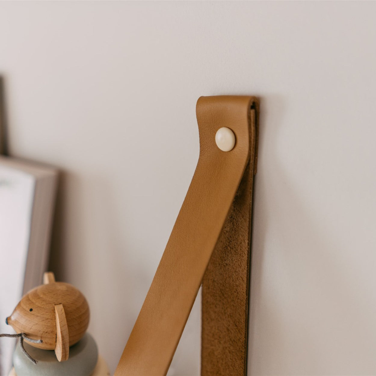a 60 cm solid pine floating shelf with light camel leather straps in a soft, elegant room setting
