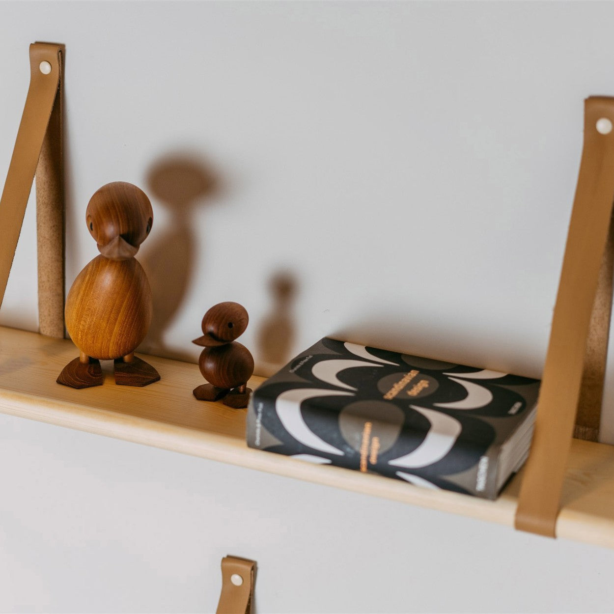 a 60 cm solid pine floating shelf with two light camel leather straps, shown in a soft, elegant close-up that highlights the wood grain and refined scandinavian detail