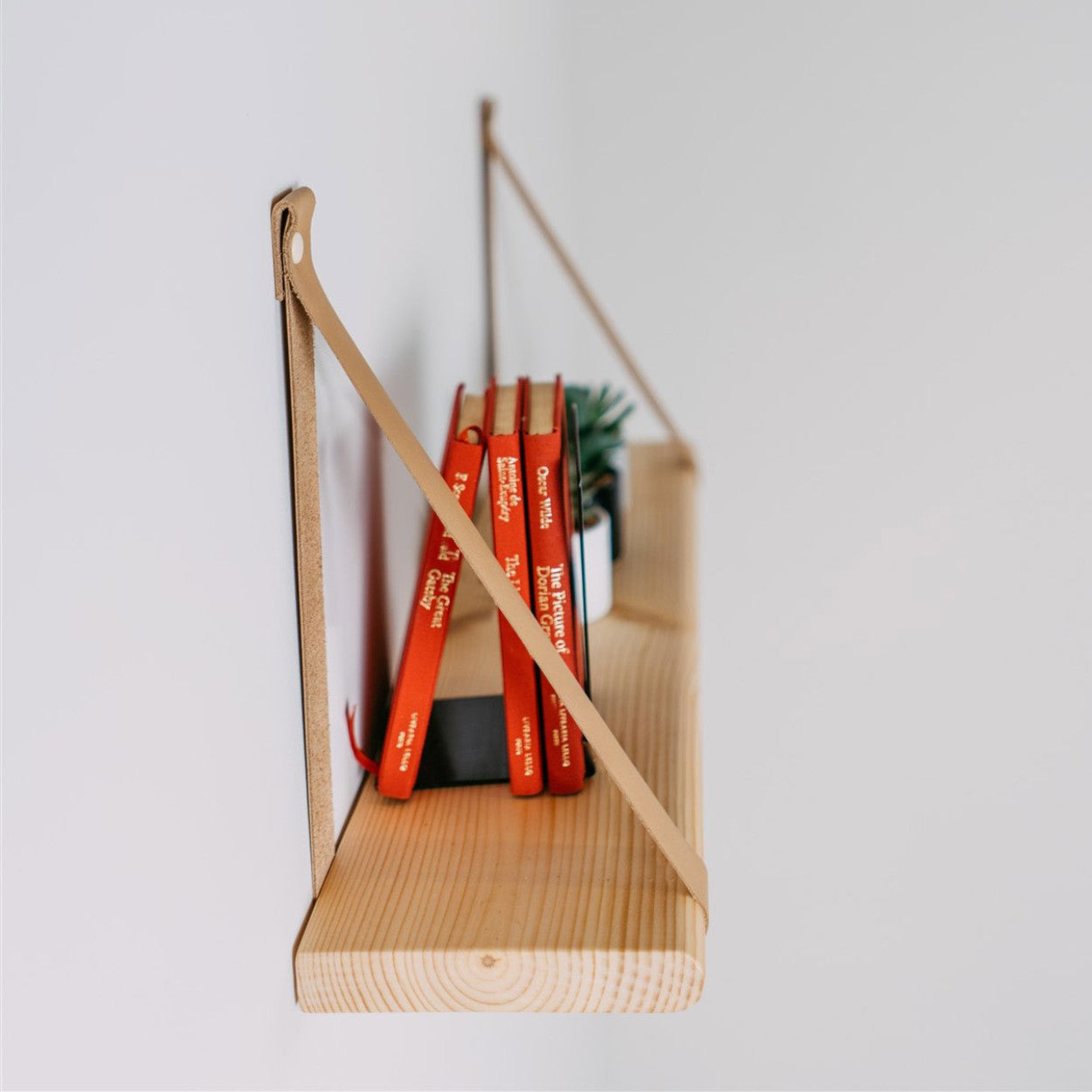 a playful 60 cm floating shelf with soft camel leather straps, shown in a child's cozy reading nook