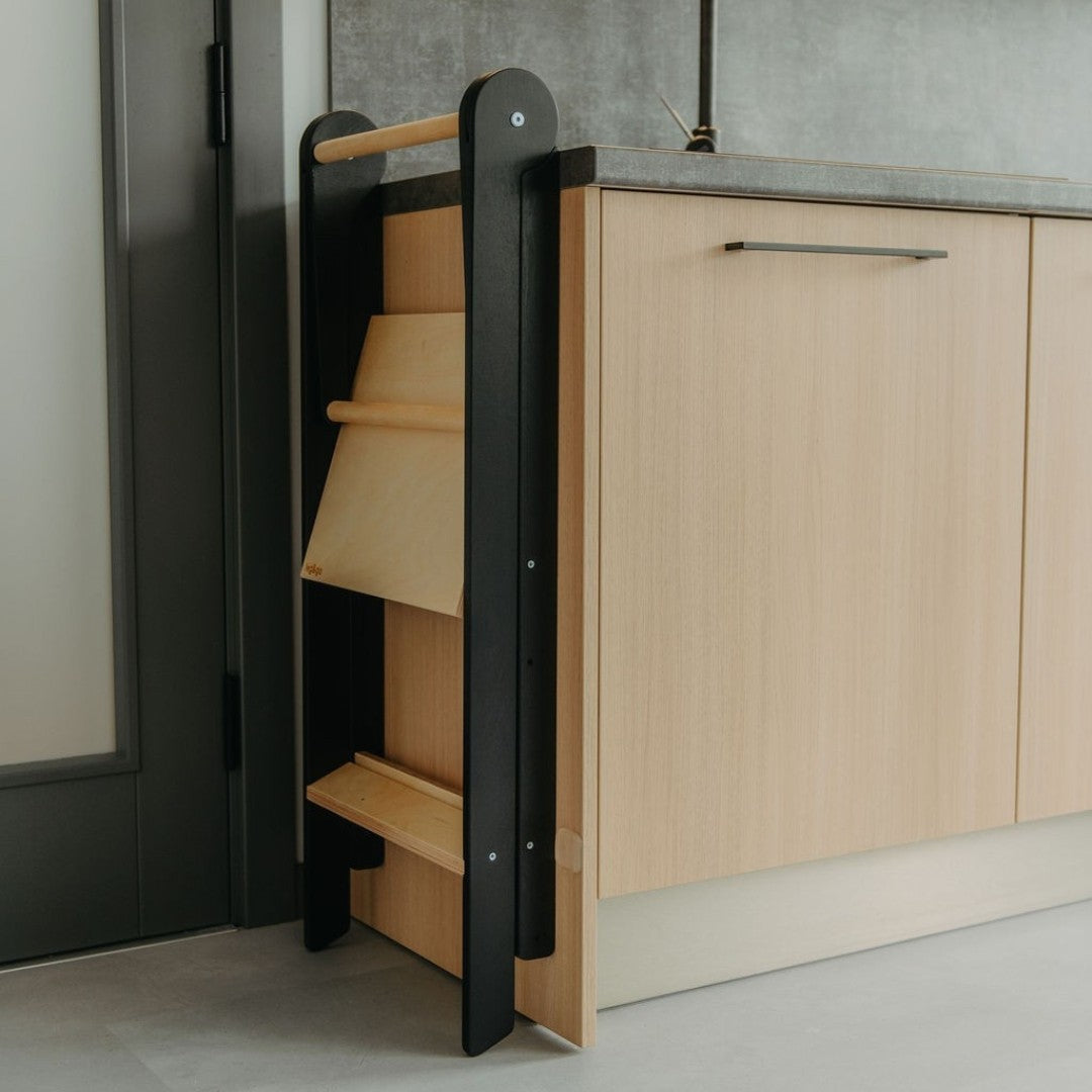 a soft-lit kitchen scene with a child safely standing at the counter in their foldable helper tower