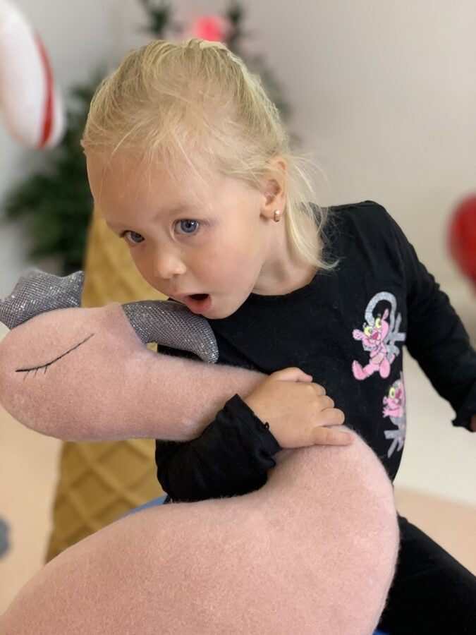 a playful pink flamingo plush with a crown tilting its head in a sunny nursery
