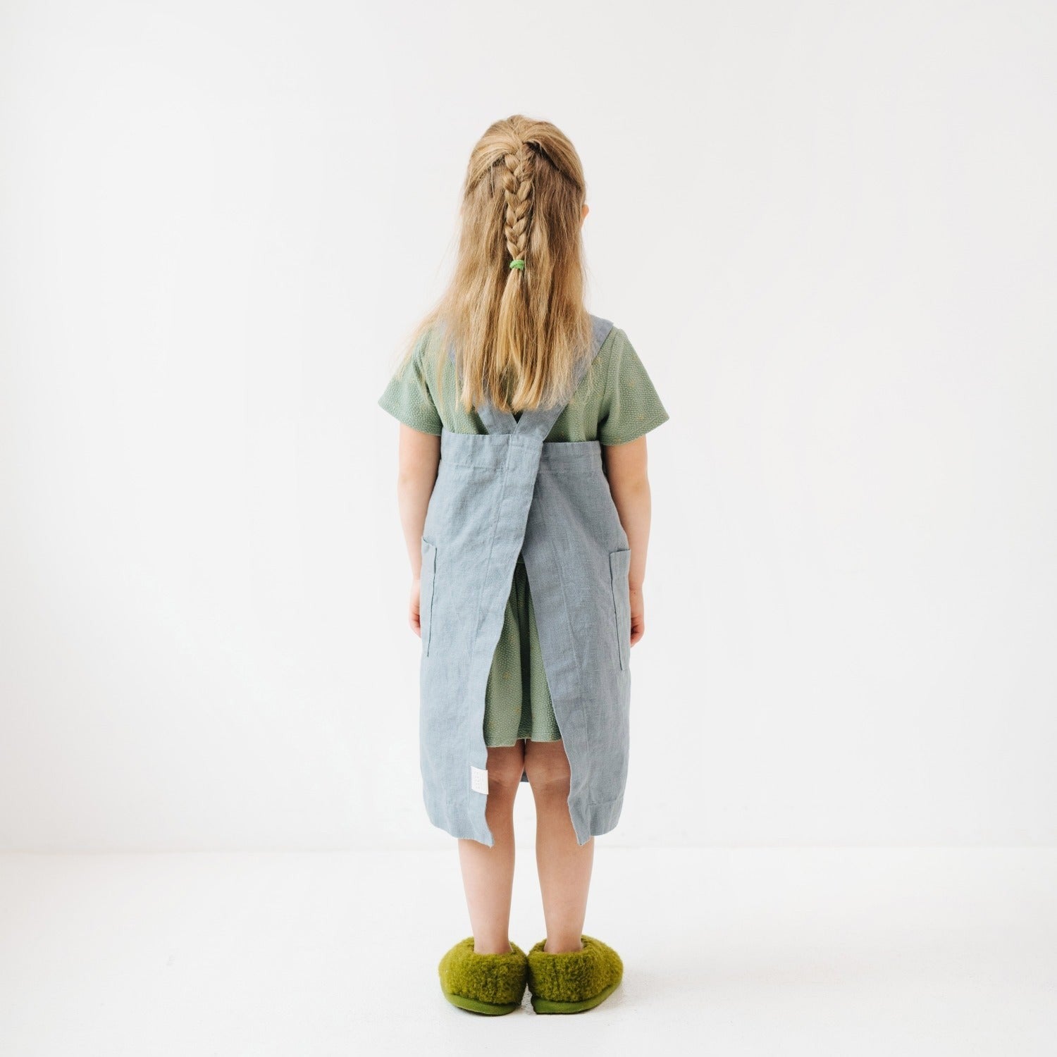 kids linen pinafore apron in blue fog showing front pockets and practical no-tie design