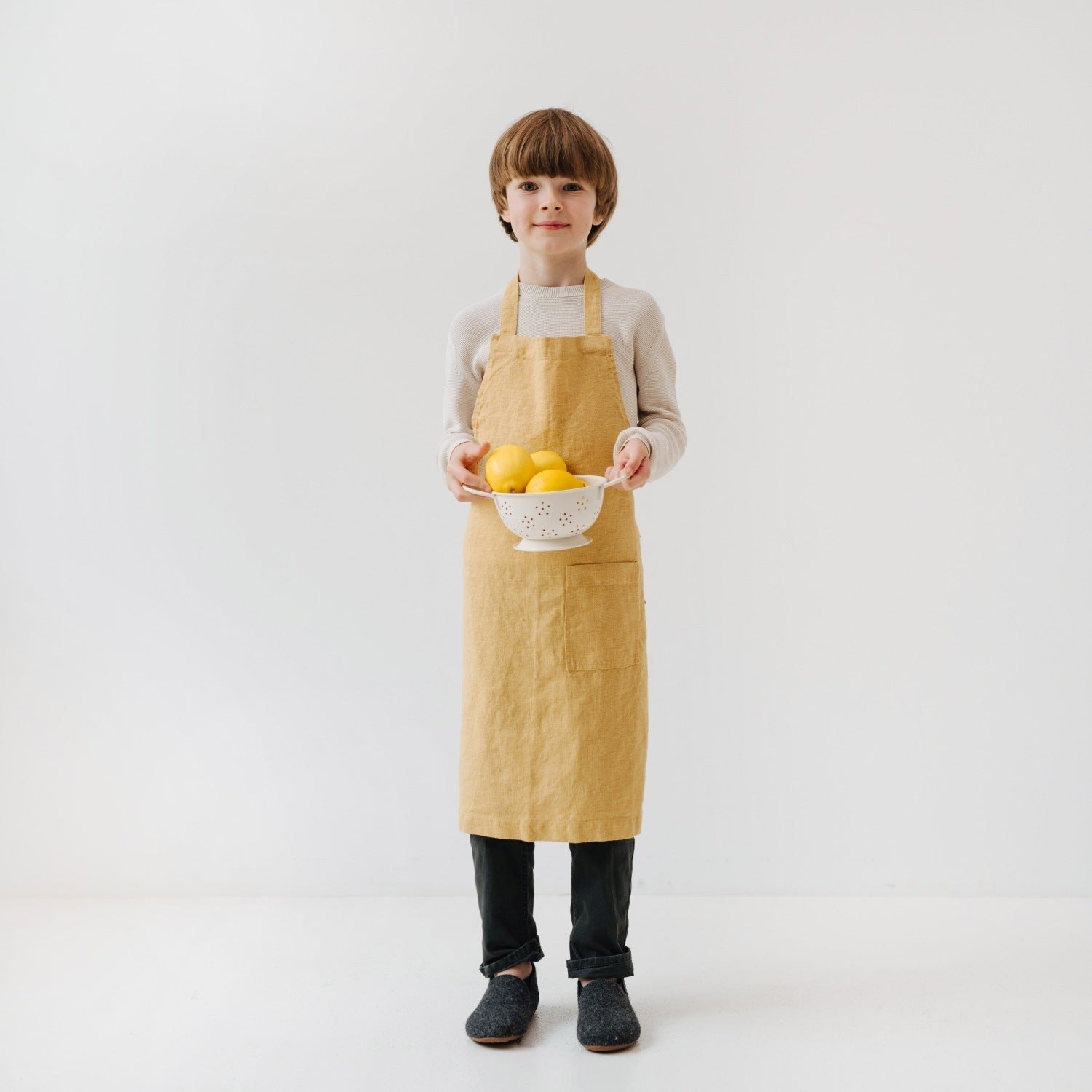 young child in a honey linen apron focused on baking with a wooden spoon