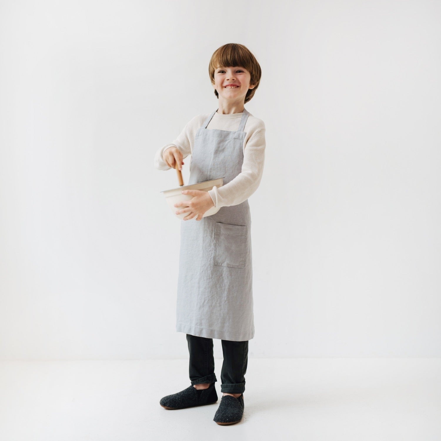 a soft grey linen kids apron with a front pocket, shown in comforting morning light