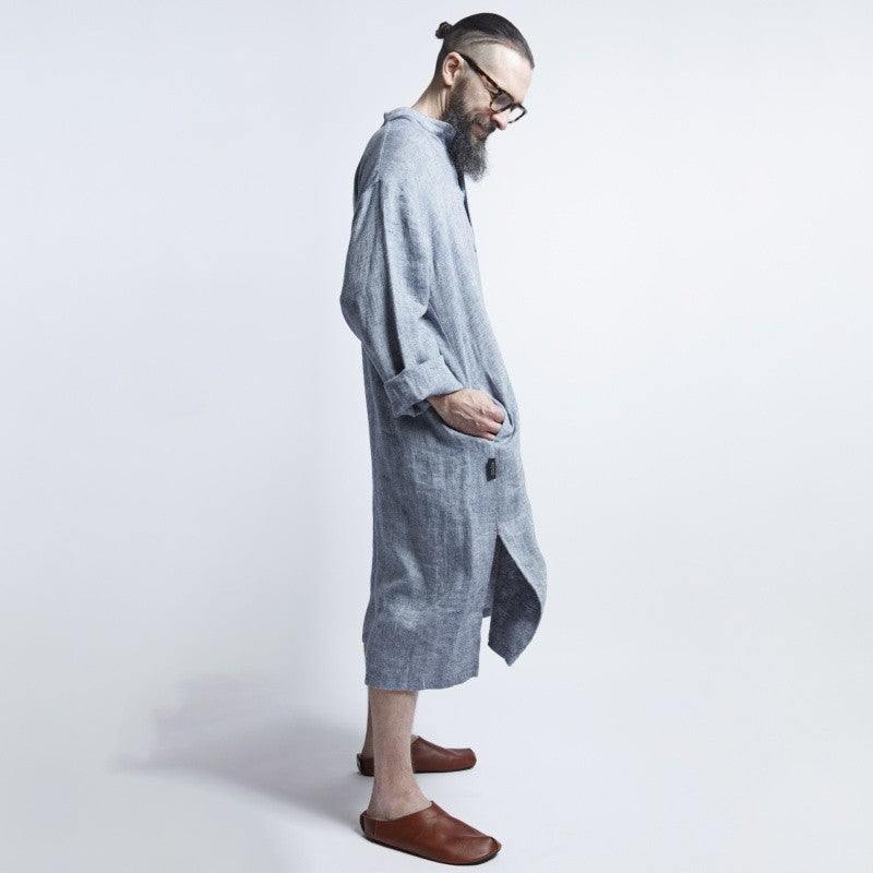 a man relaxing in a soft blue-gray linen dress, the fabric gently draped in warm afternoon light
