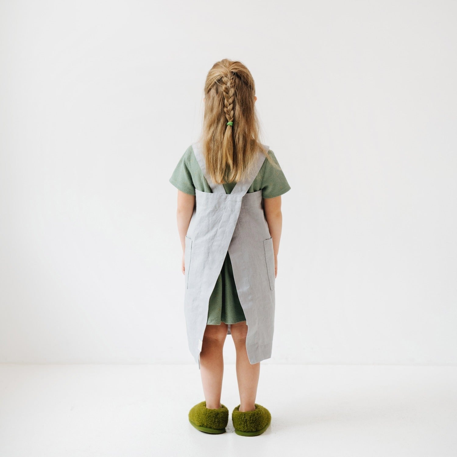 a soft grey linen kids apron with two pockets, shown in gentle morning light