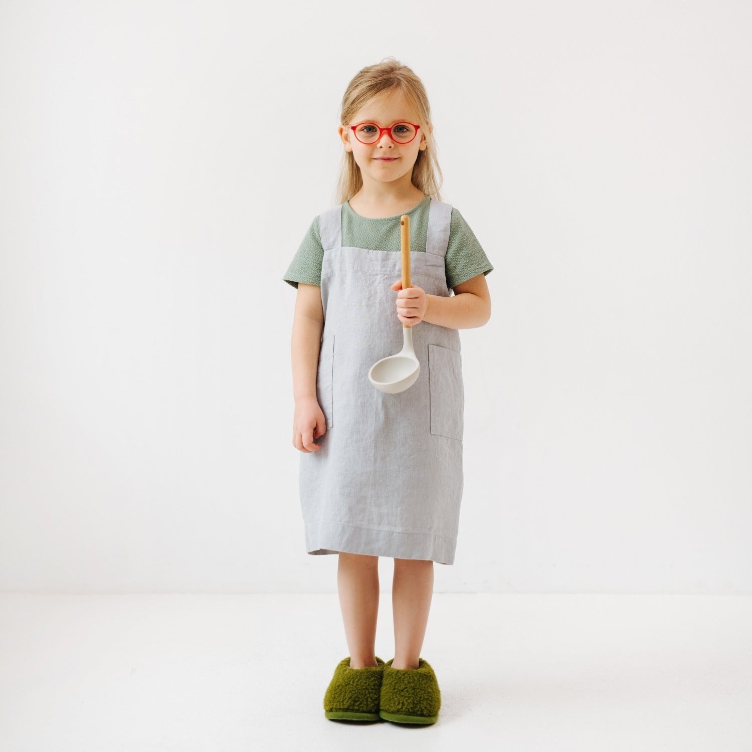 light grey linen kids apron with two deep pockets for kitchen tools, shown from a practical side angle