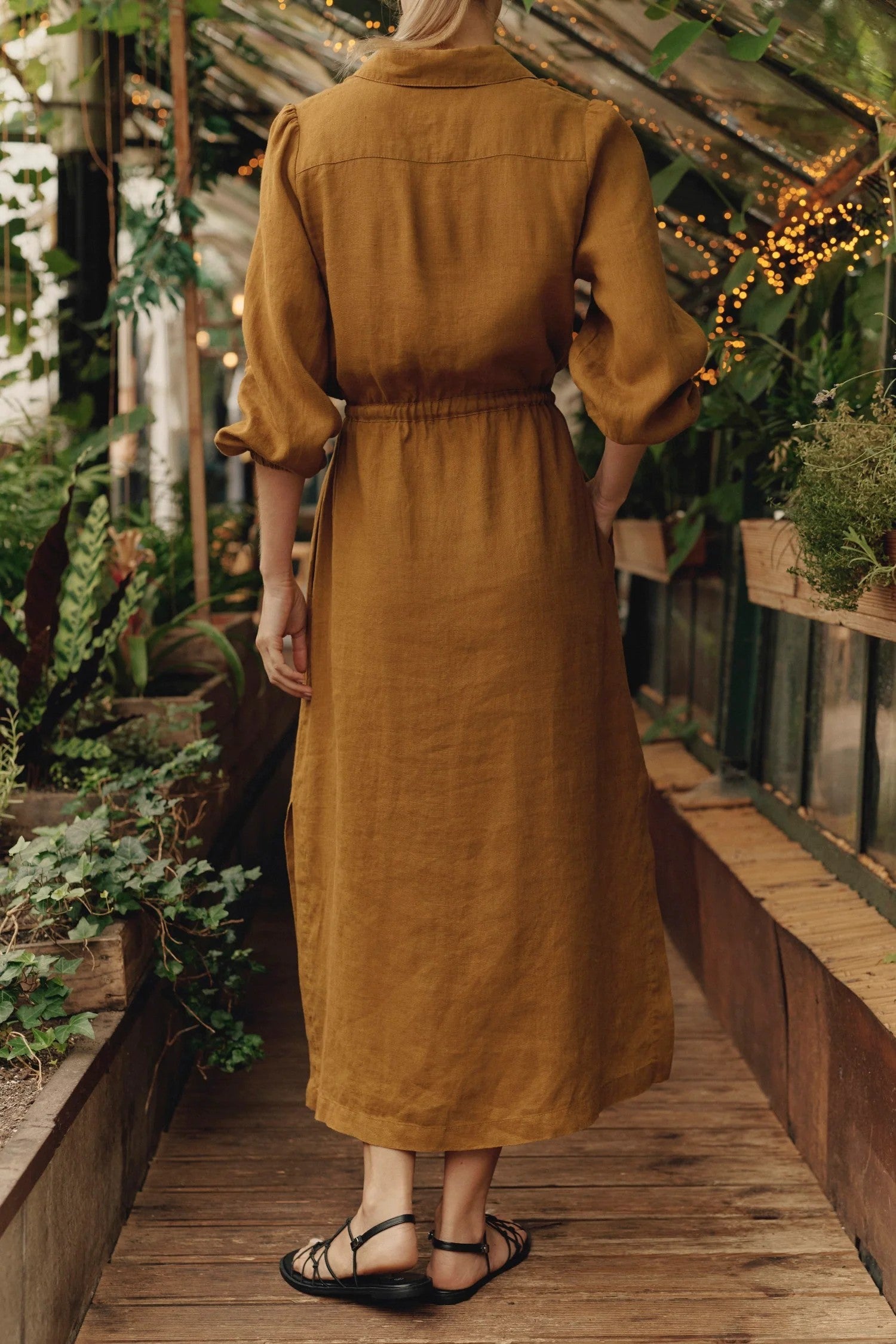 a playful twirl showing the bronze linen dress with flowing side splits and a cinched belt