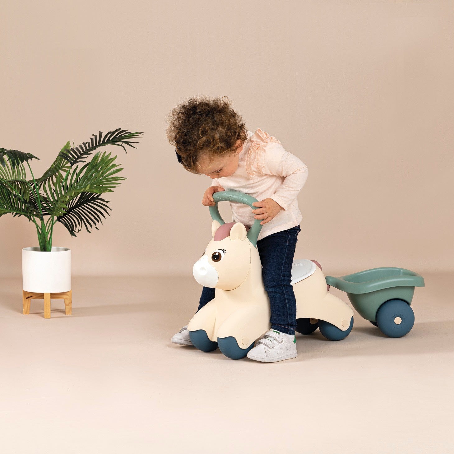 elegant side profile of a pastel ride-on pony and trailer for toddlers in a sunlit garden