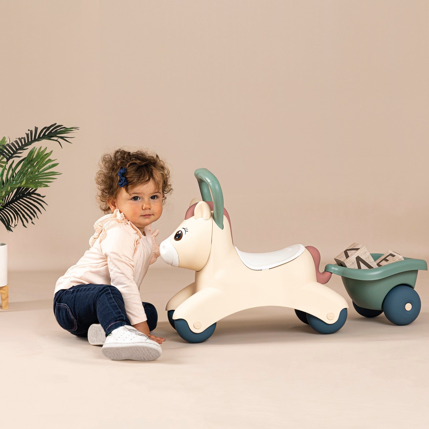 a soft pastel ride-on pony with trailer for toddlers in a cozy nursery setting