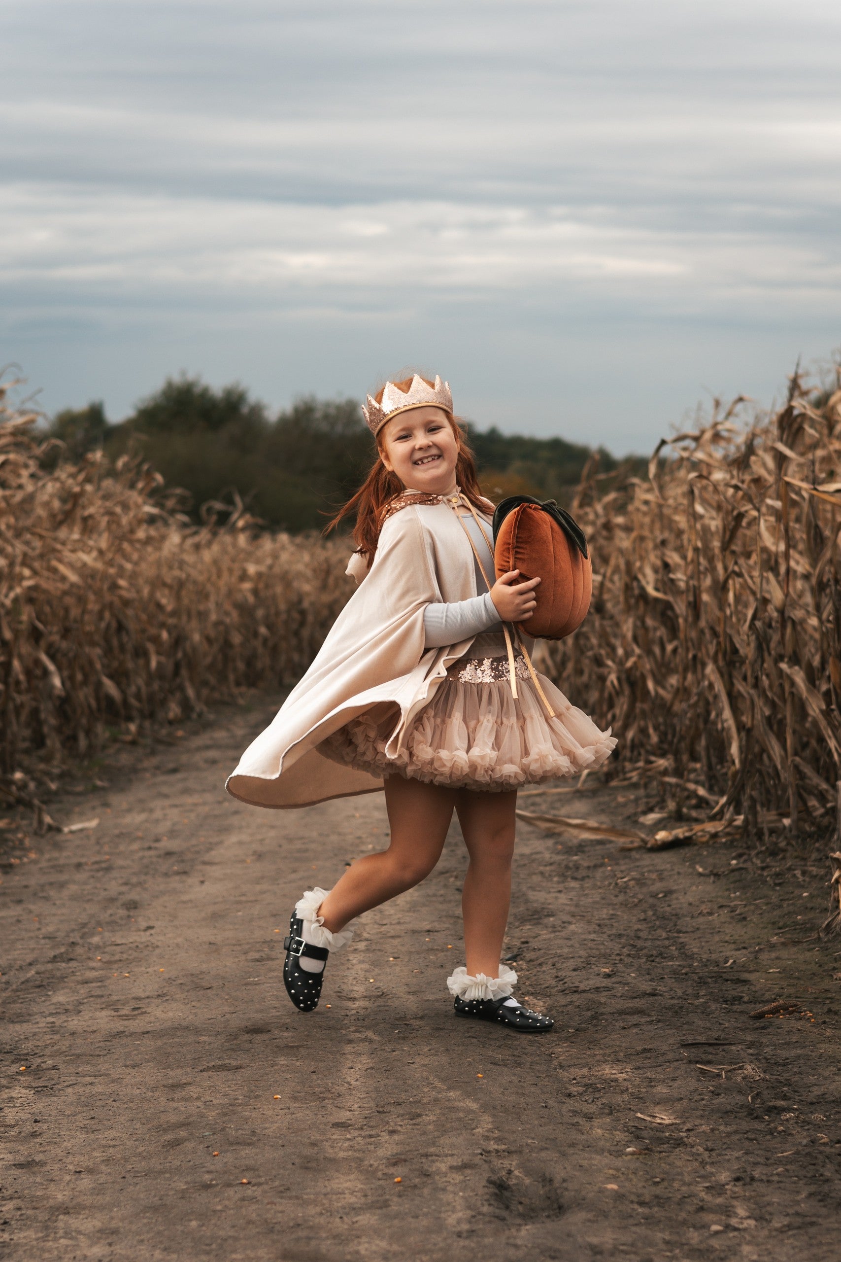 a child in a cream pearl magic cape playing outdoors, the velour shimmering in the sunlight