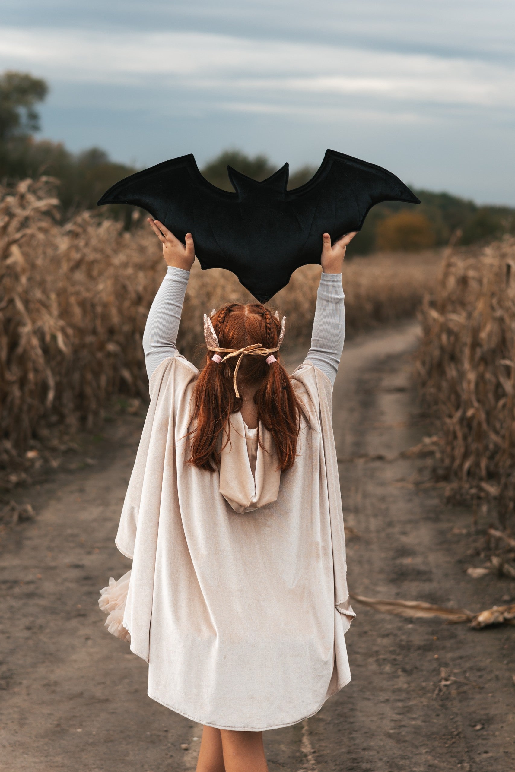 child in cream pearl magic cape with hood up, playing in a sunlit garden