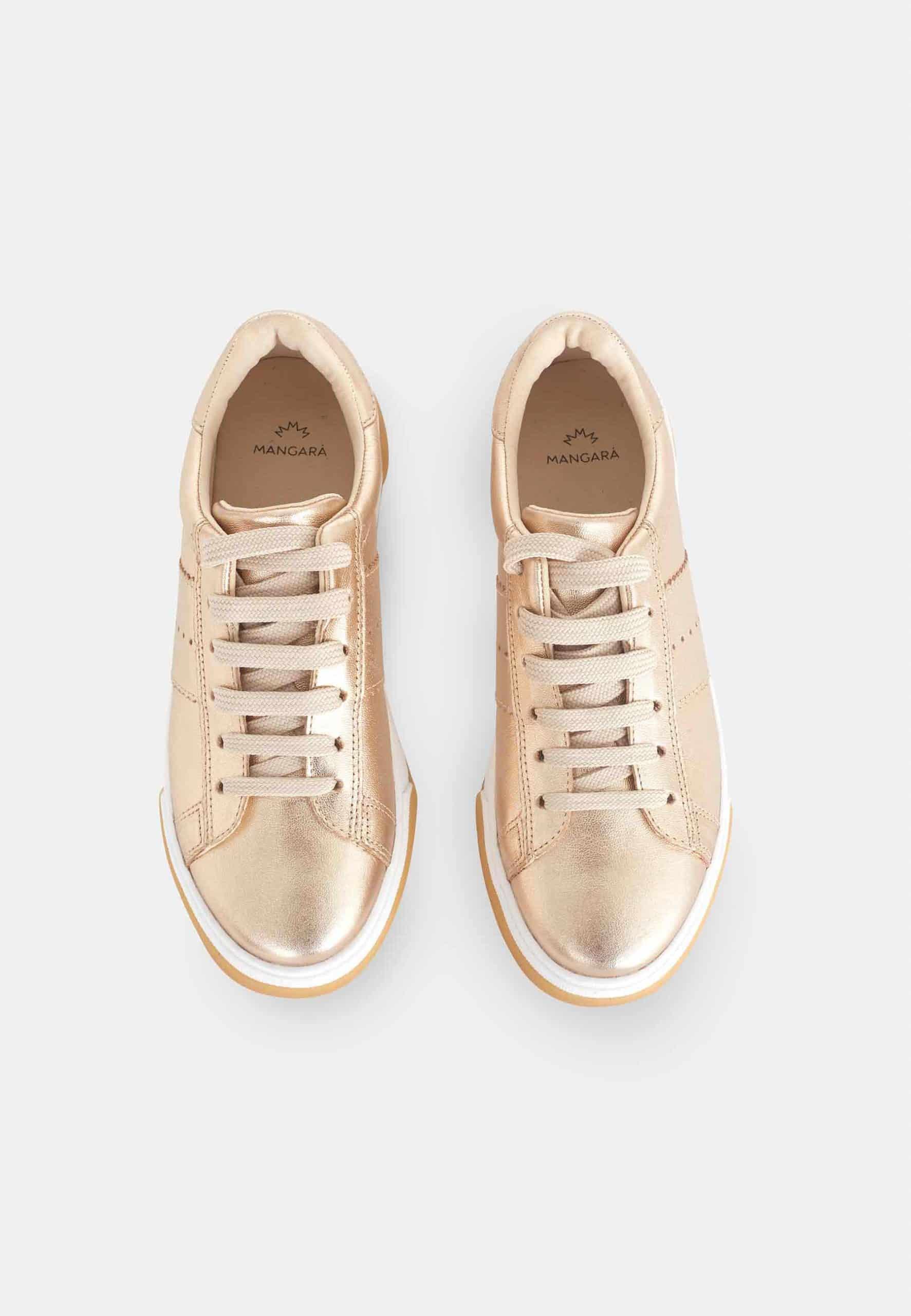 playful close-up of women's golden metallic leather sneakers on a vibrant city sidewalk