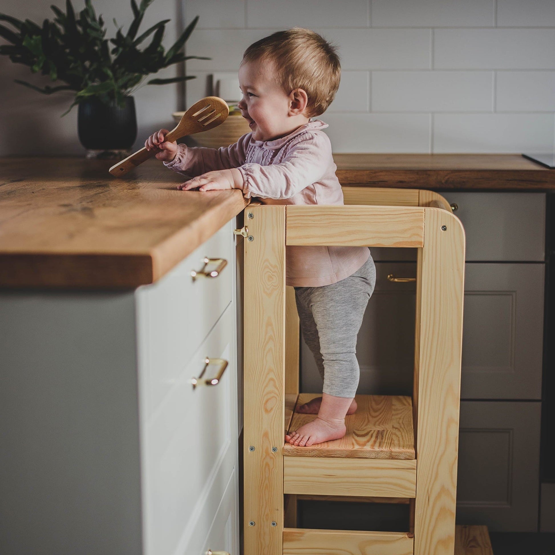 confident toddler standing on a sturdy wooden kitchen helper stool at counter