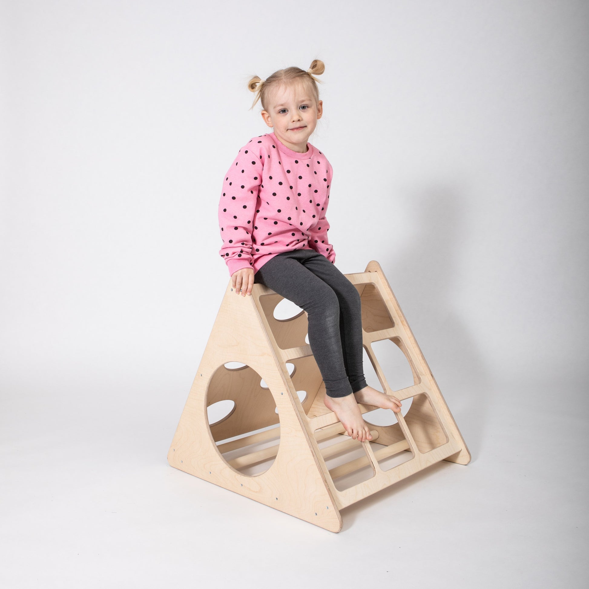 a toddler's hand gripping the sturdy birch rung of a montessori climber in warm indoor light