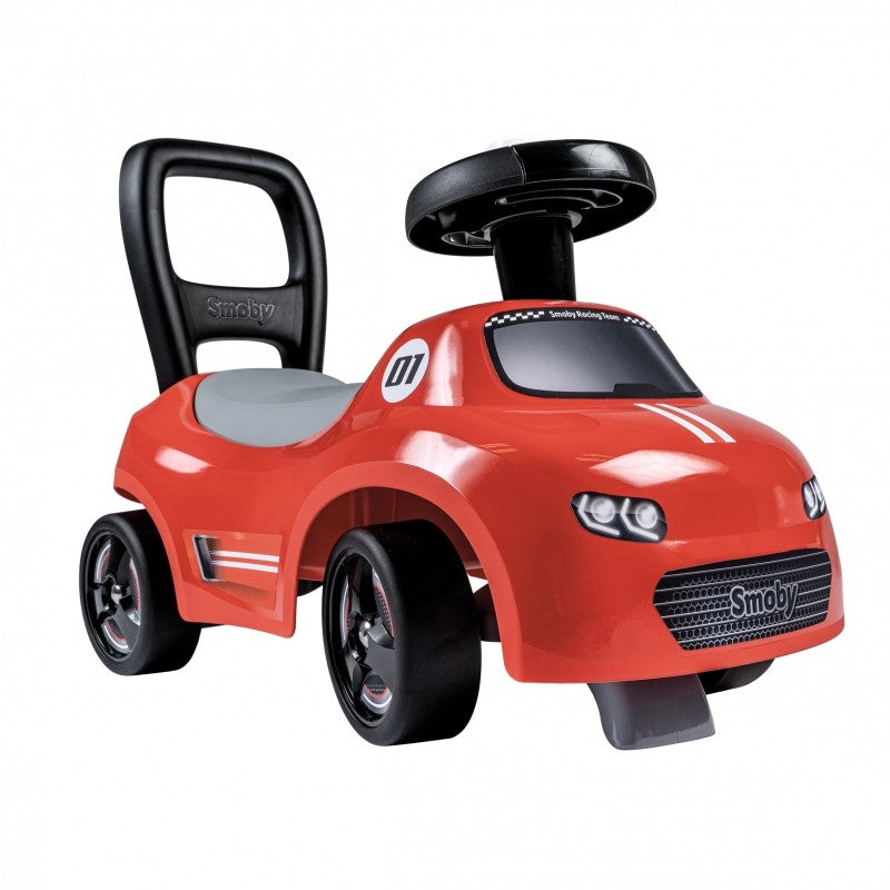 a toddler playing with a red smoby ride-on car with horn in a sunny garden