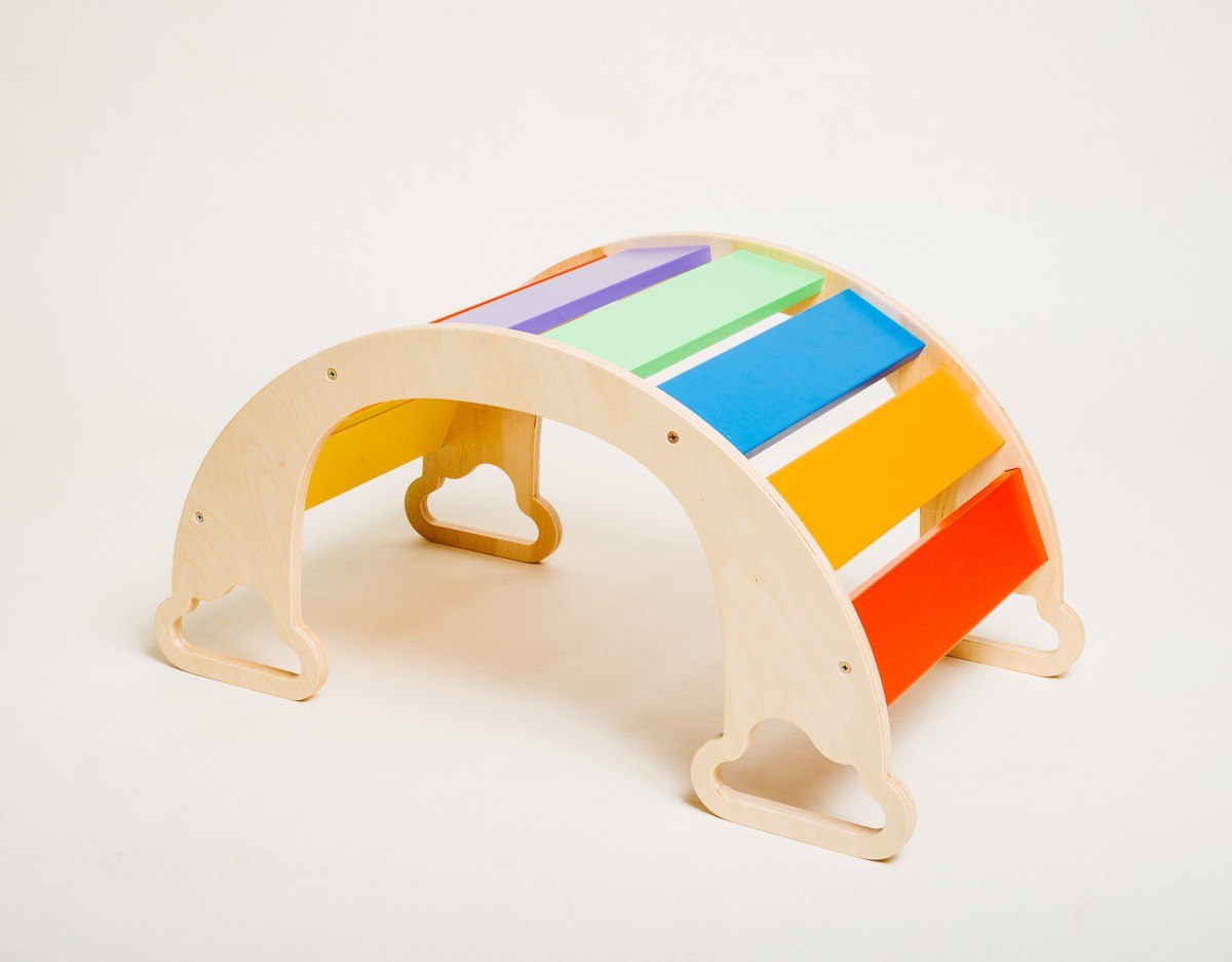 a toddler using the rainbow climber as a slide in a cozy indoor playroom