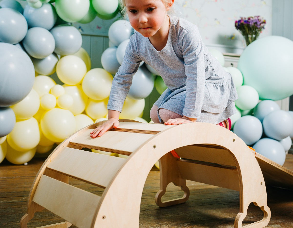 a child's hand on the birch plywood rainbow climber, showcasing its smooth functional design