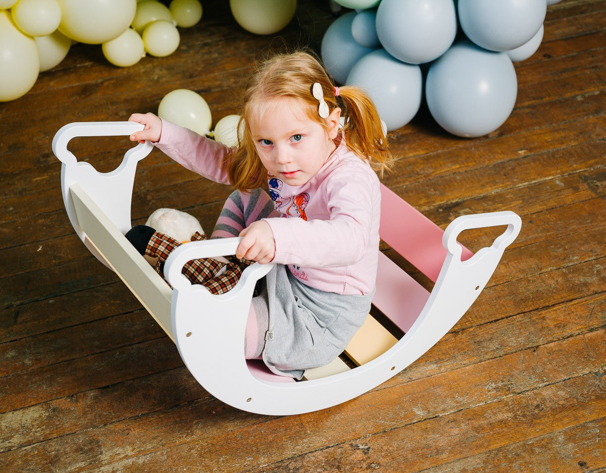 a child's hand on the birch plywood rainbow climber swing in warm indoor light