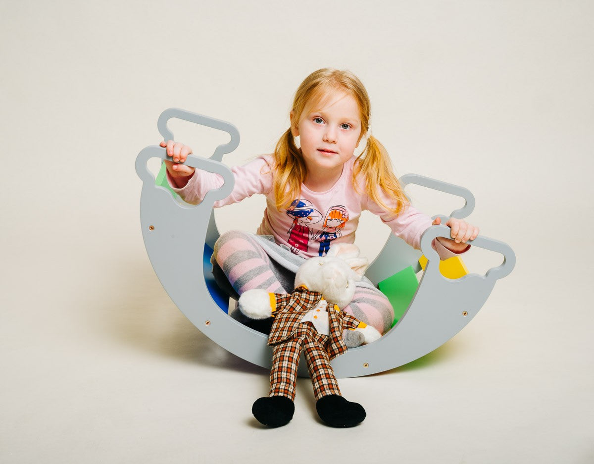 a child using the rainbow climber as a slide in a sunlit playroom