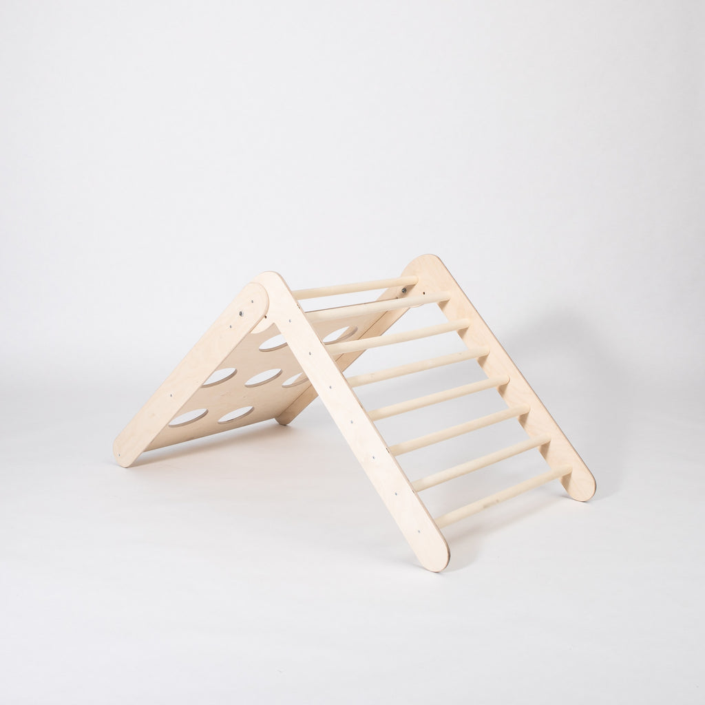a toddler climbing the foldable montessori triangle in a sunlit playroom, showcasing its adjustable slope and sturdy birch frame
