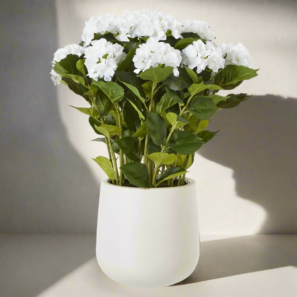 Luxury white faux hydrangea arrangement with velvety petals and lush foliage in a classic farmhouse-style vase by Sostter at brixbailey.com