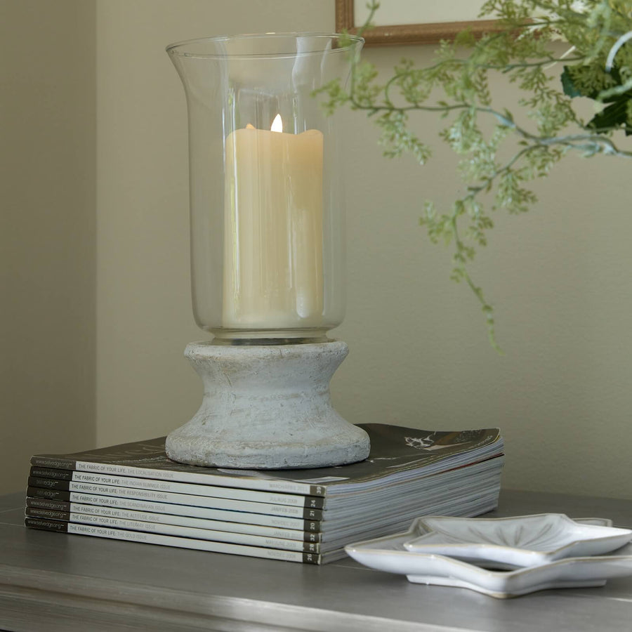 Handcrafted cream hurricane lantern with stone-effect base and antiqued patina, casting warm LED candlelight glow. by Sostter at brixbailey.com