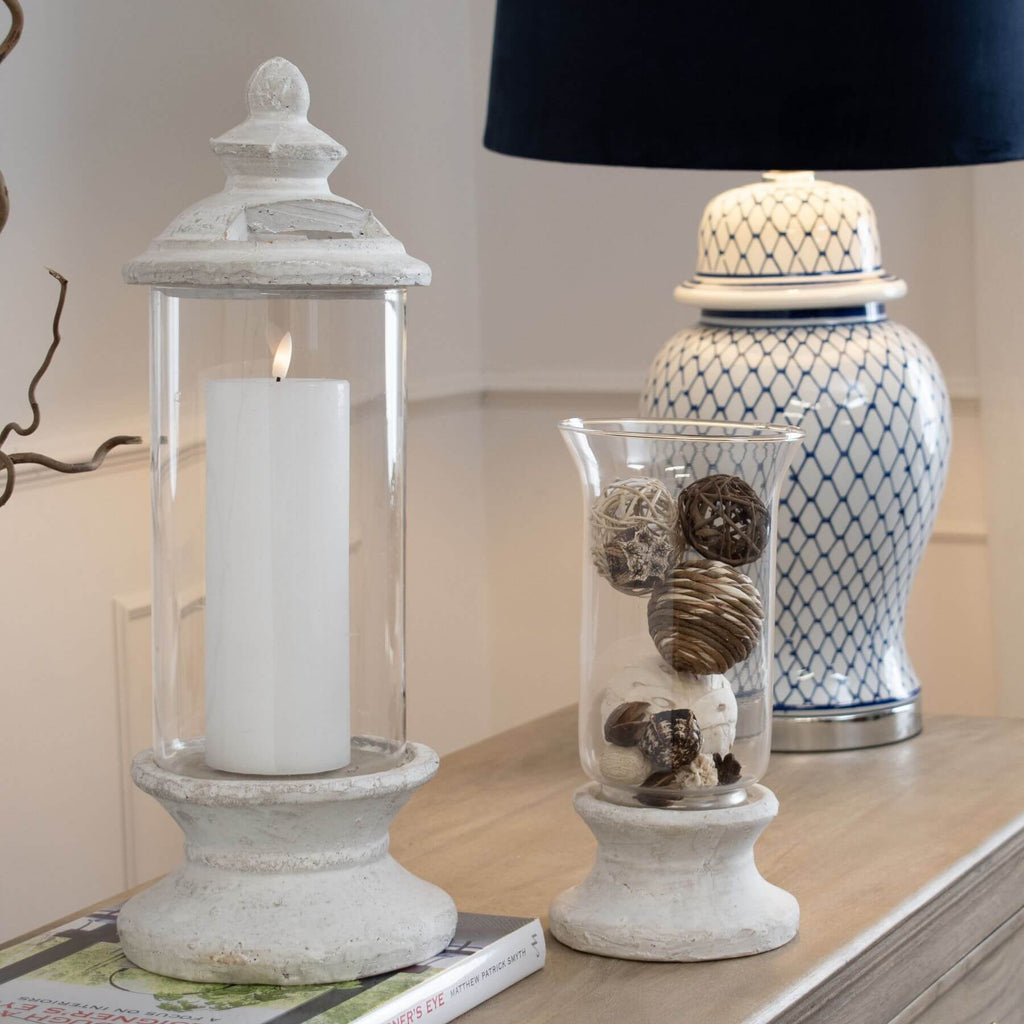 Handcrafted cream hurricane lantern with stone-effect base and antiqued patina, diffusing warm LED candlelight. by Sostter at brixbailey.com