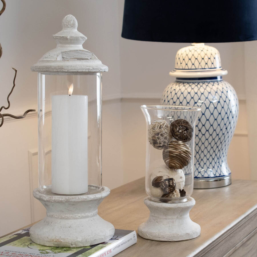 Handcrafted cream hurricane lantern with stone-effect base and antiqued patina, diffusing warm LED candlelight. by Sostter at brixbailey.com