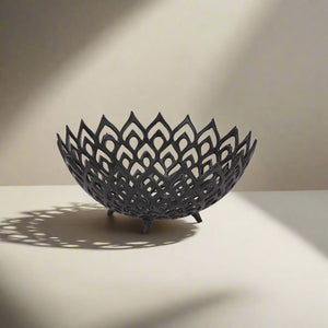 Matte black perforated steel bowl with intricate lattice design, casting dynamic light and shadow patterns by RoomLondon at brixbailey.com