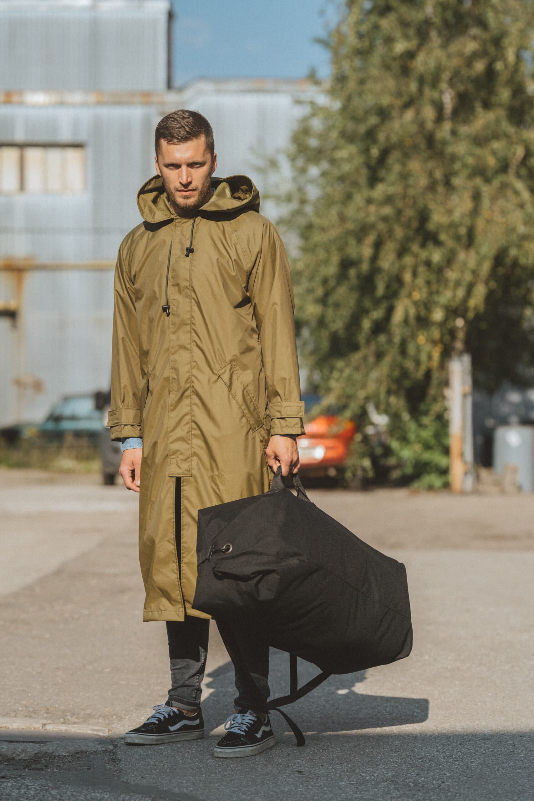 confident man in military green waterproof rain jacket, bold stance against stormy backdrop