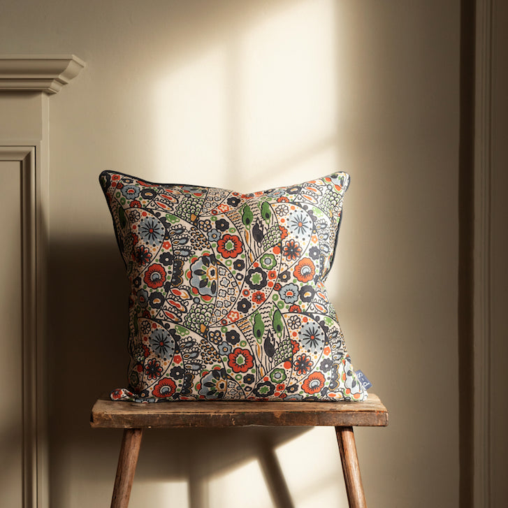 Decorative pillow with a floral pattern on a wooden stool against a beige wall from independent brands at Sostter