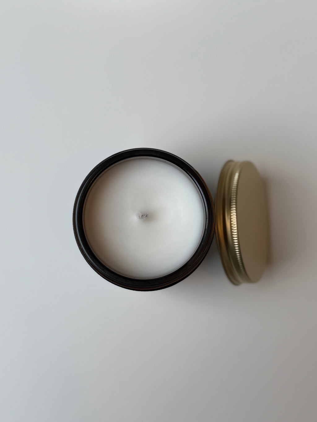 White candle in a black container with a gold lid on a light gray background