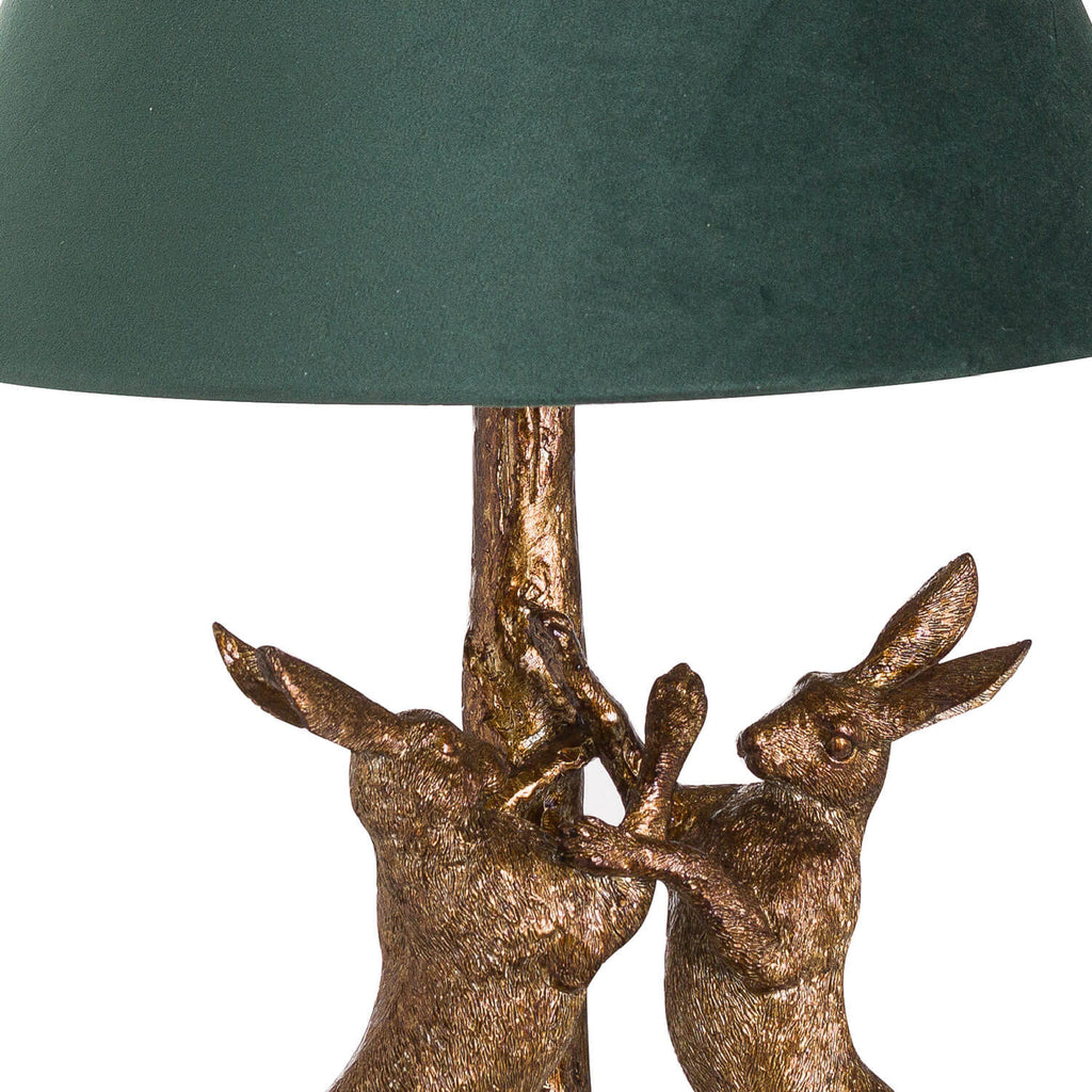 Antique gold marching hare lamp with green velvet shade, handcrafted resin sculpture casting warm ambient glow when lit. by Sostter at brixbailey.com