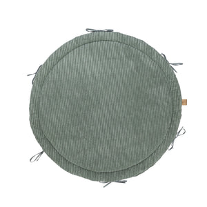 soft olive green baby nest with braided bumper on a cozy nursery rug