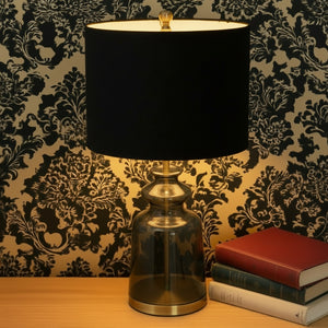 Table lamp with black shade and smoked glass base against a decorative wallpaper background