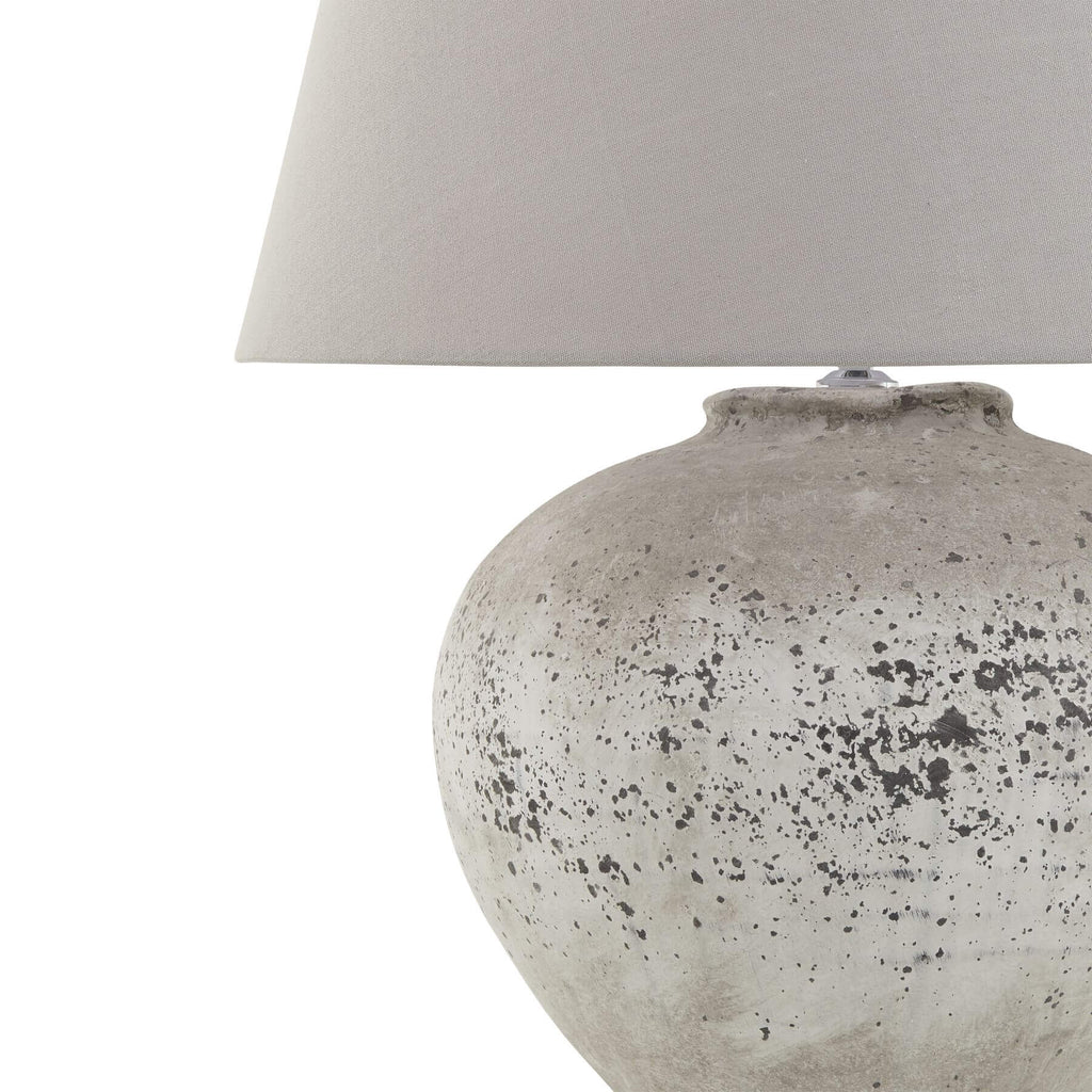Handcrafted stone-effect ceramic lamp with light grey fabric shade, natural textured base, and warm ambient glow. by Sostter at brixbailey.com