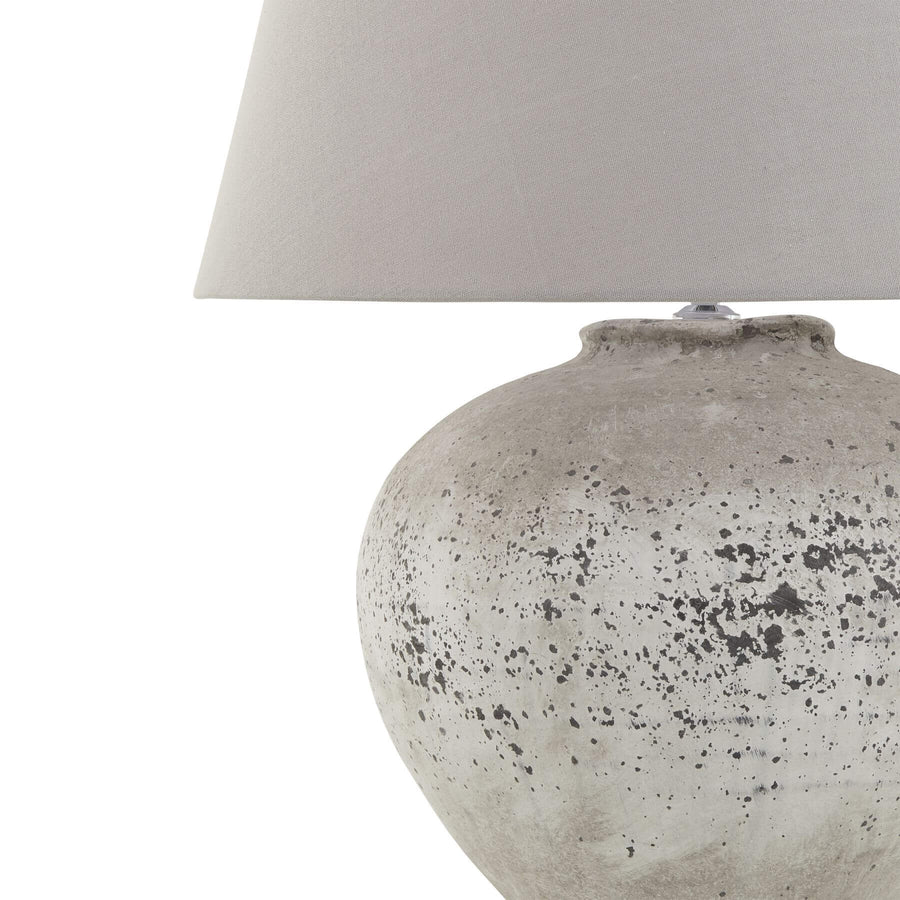 Handcrafted stone-effect ceramic lamp with light grey fabric shade, natural textured base, and warm ambient glow. by Sostter at brixbailey.com