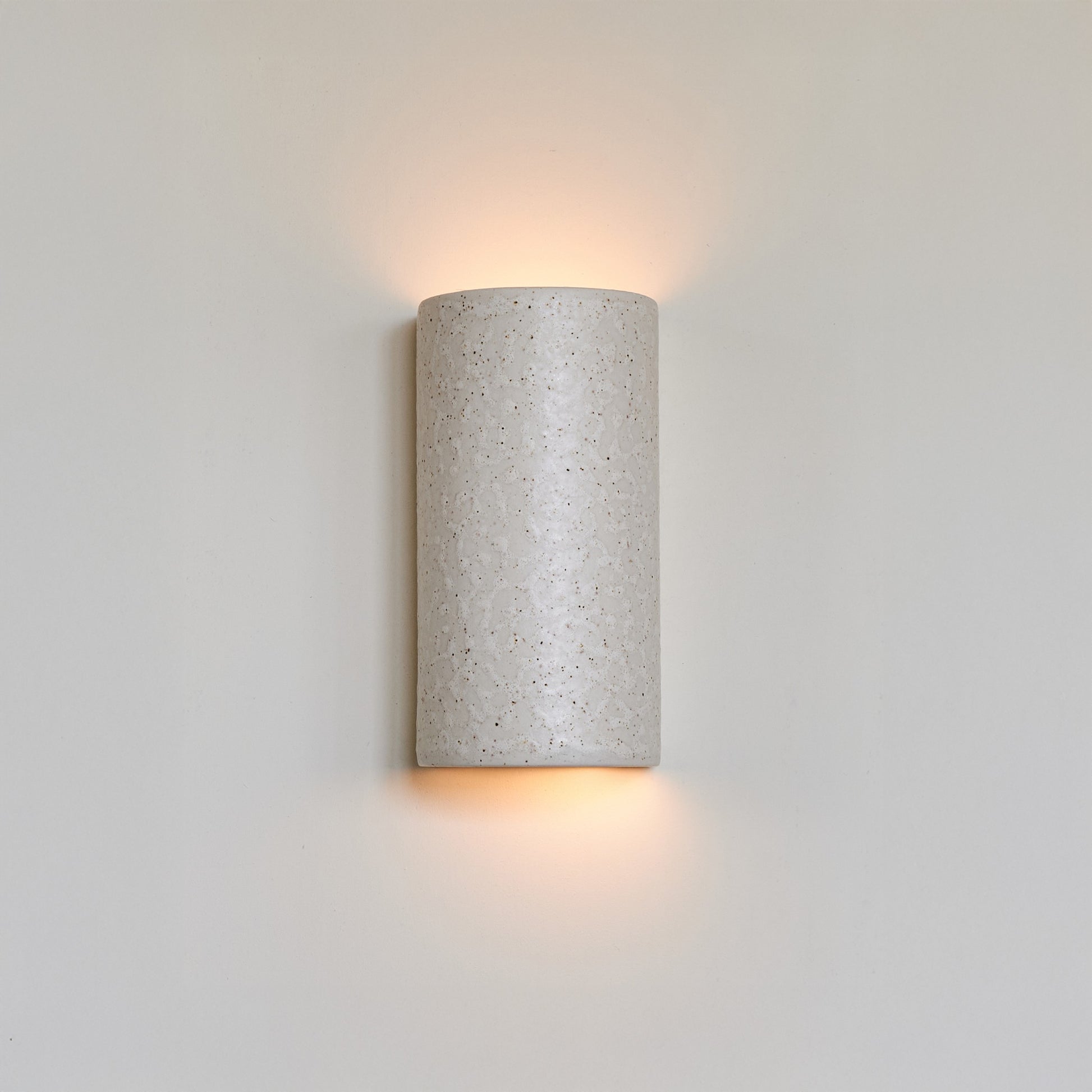 a soft beige ceramic wall light with a gentle brown speckled glaze, casting a warm and comforting glow in a nursery