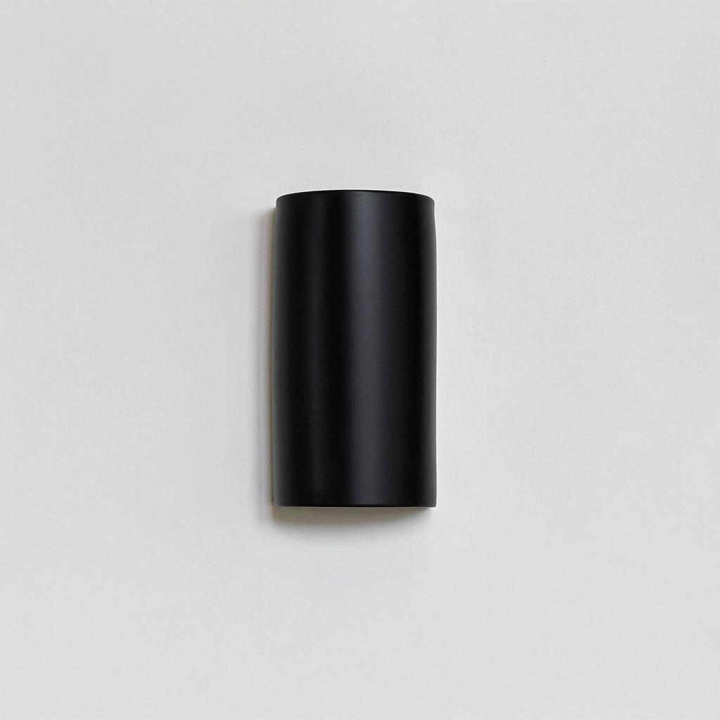 elegant black ceramic wall light casting a cinematic glow on a textured wall