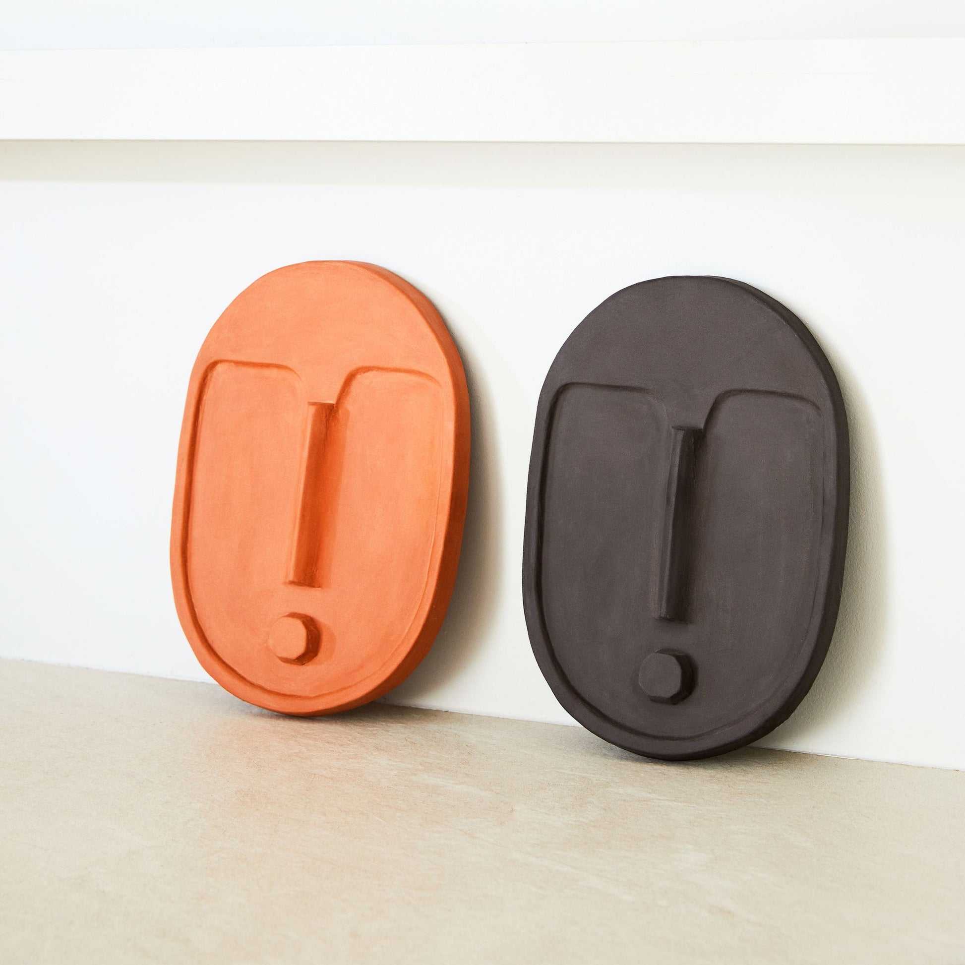 softly lit anthracite grey ceramic wall mask with warm terracotta glaze, casting gentle shadows on a neutral wall