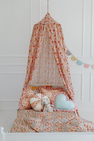 soft cotton quilted blanket and pillow set in summer garden patchwork, draped gently over a wooden chair