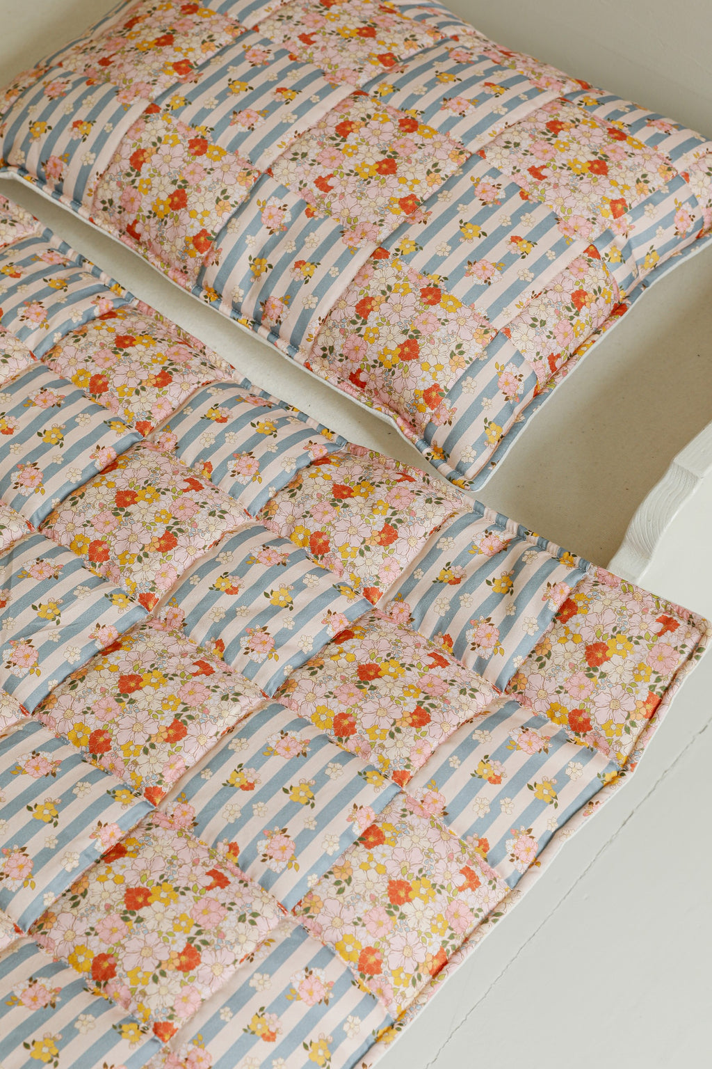 elegant summer garden quilted blanket and pillow set draped over a rustic wooden chair, soft pastel patchwork patterns