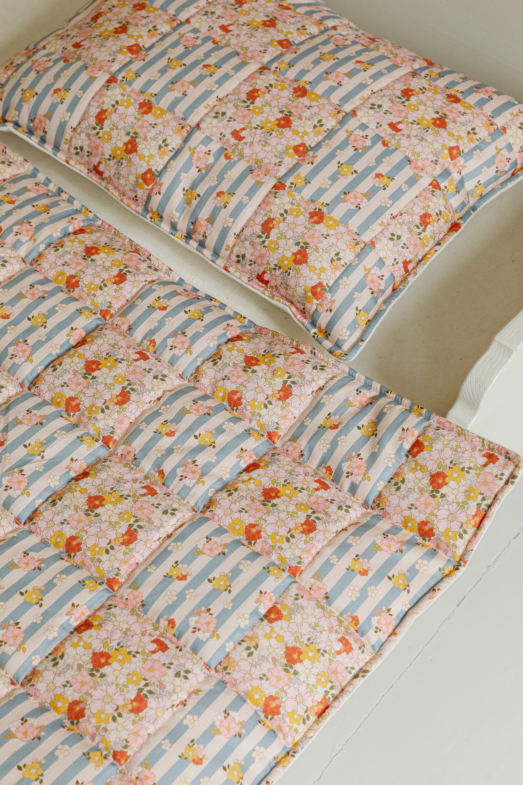 elegant summer garden quilted blanket and pillow set draped over a rustic wooden chair, soft pastel patchwork patterns