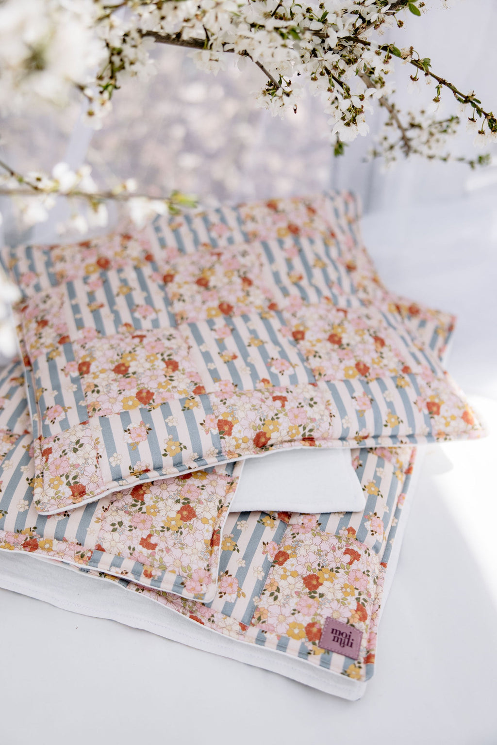 functional cotton quilted blanket and pillow set laid flat on a wooden floor, showcasing summer garden patchwork pattern