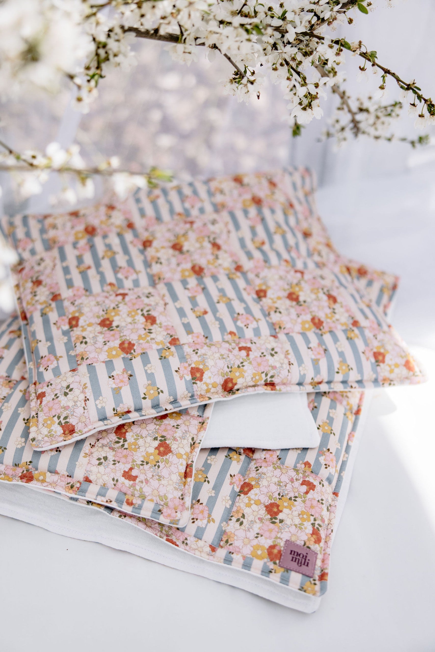 functional cotton quilted blanket and pillow set laid flat on a wooden floor, showcasing summer garden patchwork pattern